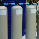 four beige tanks in an outdoor water treatment setup with blue piping